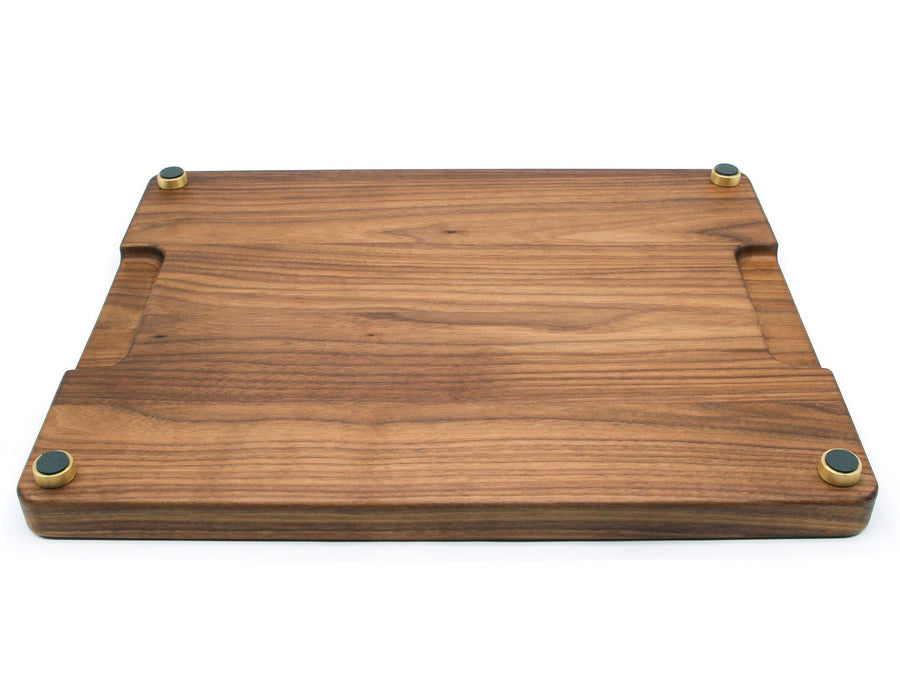 Underside of a wooden cutting board showing four installed brass feet