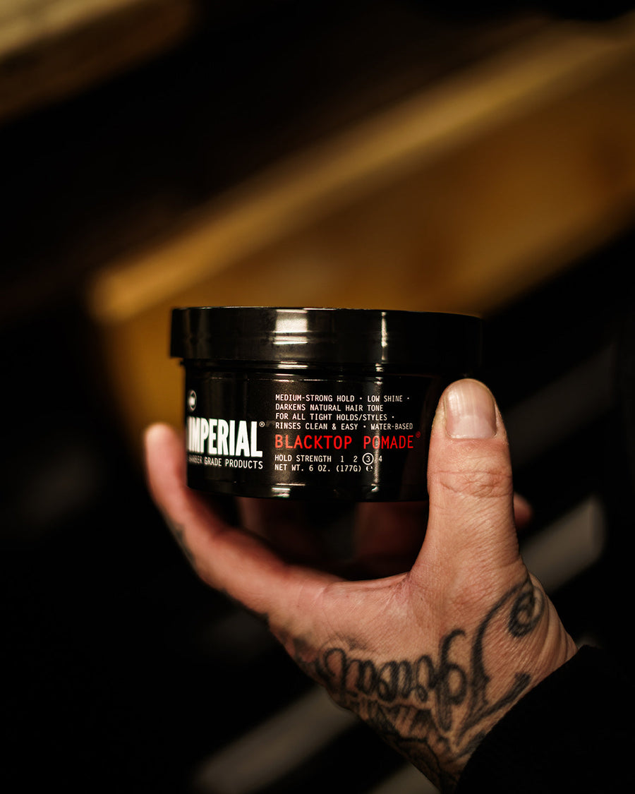 Blacktop Tinted Pomade — Blacktop Pomade jar held near a barber station