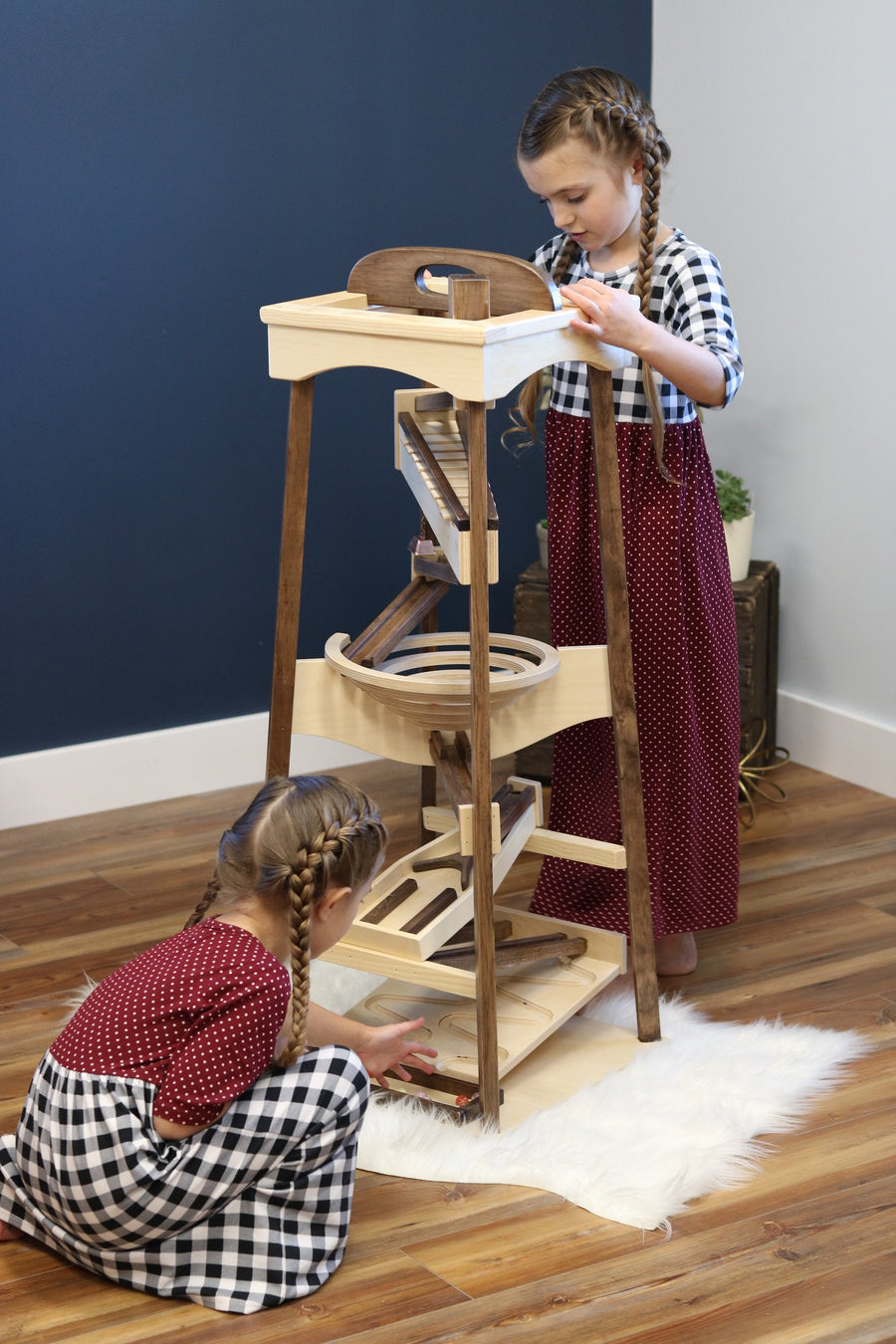 Child standing beside a wooden pyramid marble run