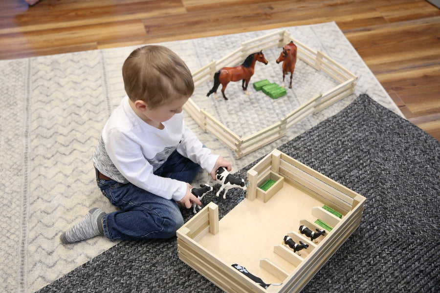 Child arranging toy animals inside a wooden miniature stockyard