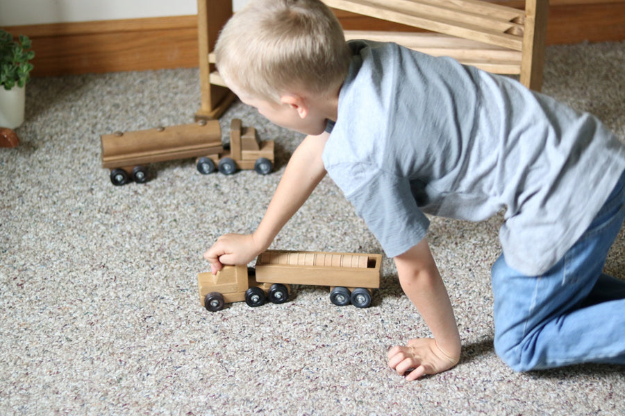 Child playing with a wooden barrel truck and trailer