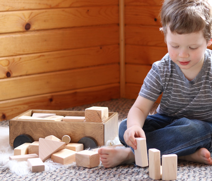 Child stacking wooden blocks beside a small pull wagon
