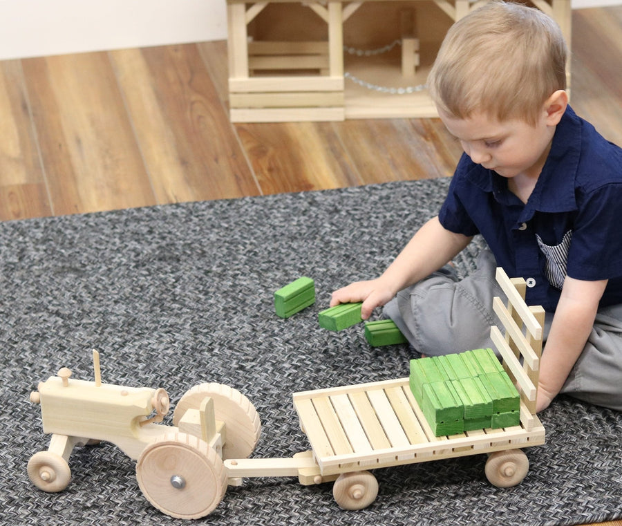Child playing with a wooden tractor, hay wagon and hay bales