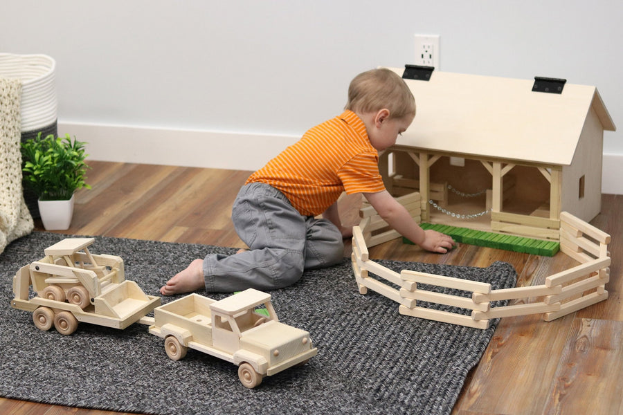 Child playing with a wooden pickup, equipment trailer and skid loader
