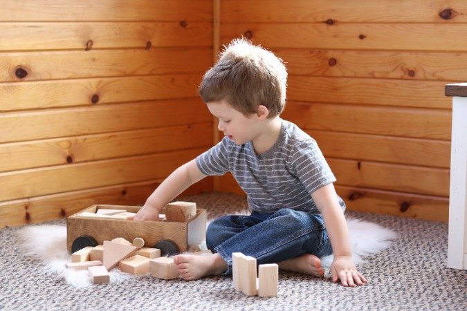 Child stacking wooden blocks beside a small pull wagon