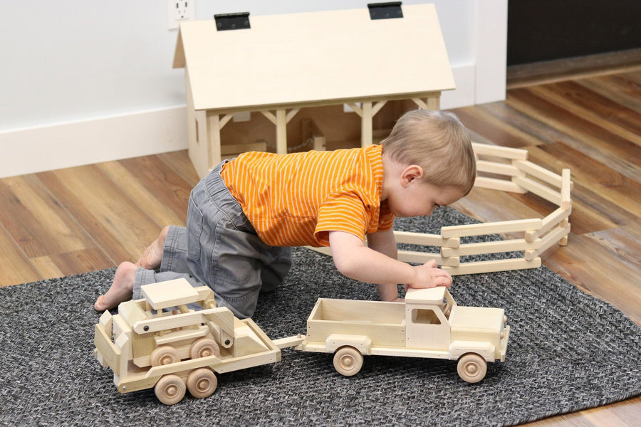 Child playing with a wooden pickup, equipment trailer and skid loader