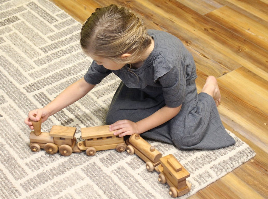 Child playing with a linked wooden toy train on a rug