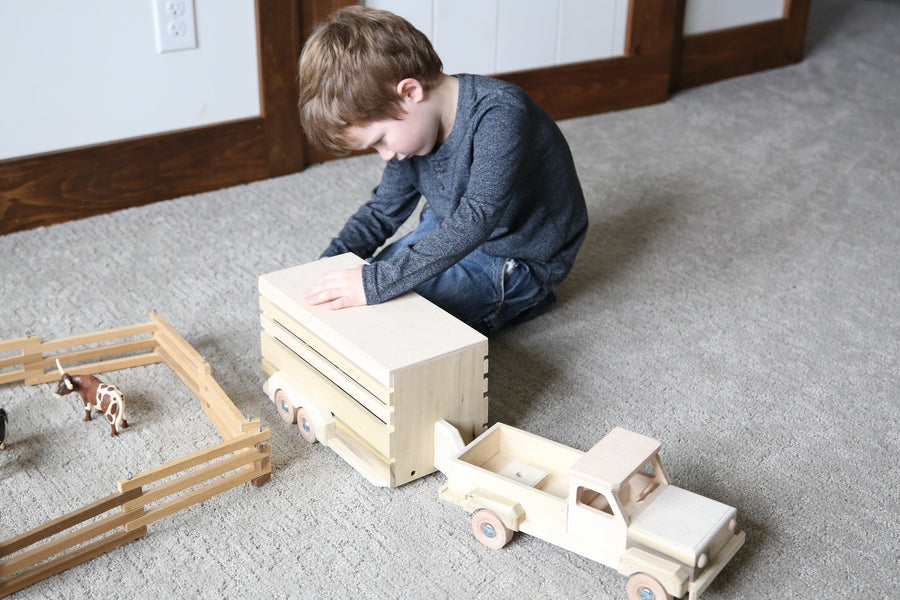Child playing with a wooden pickup and horse trailer