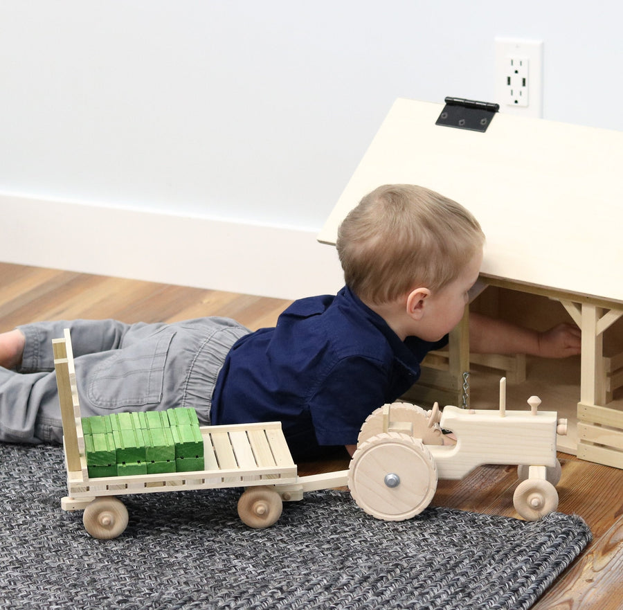 Child playing with a wooden tractor, hay wagon and hay bales