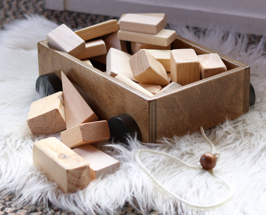 Wooden pull wagon with unfinished building blocks spilling beside it