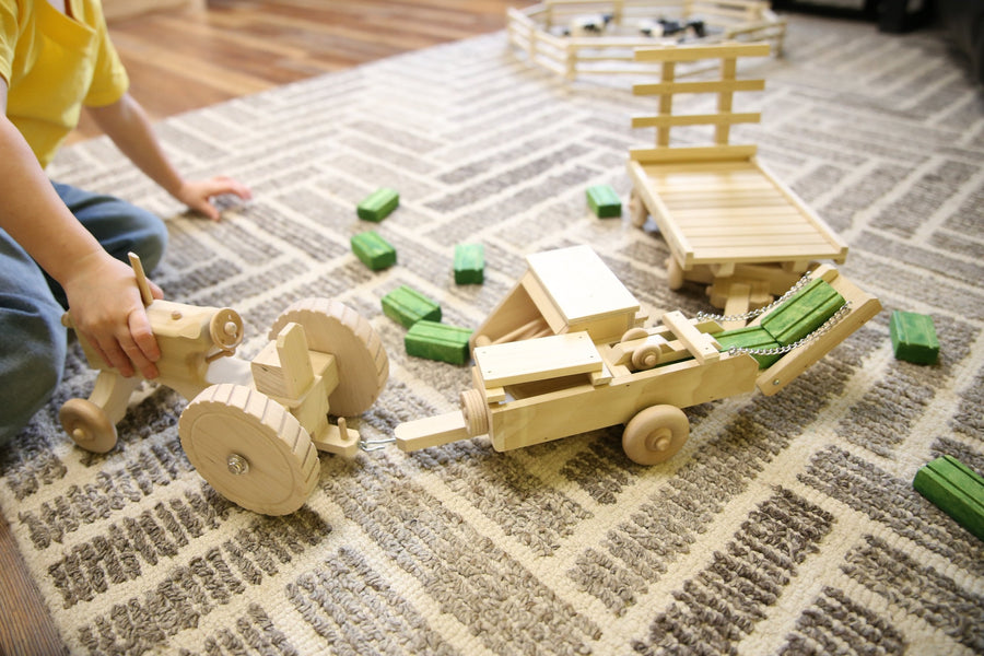 Child playing with a wooden tractor, baler and hay wagon