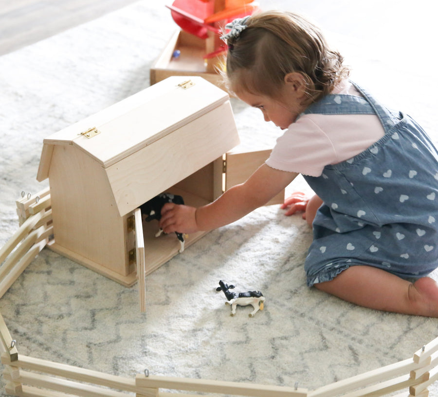 Child playing with a miniature wooden hip-roof barn
