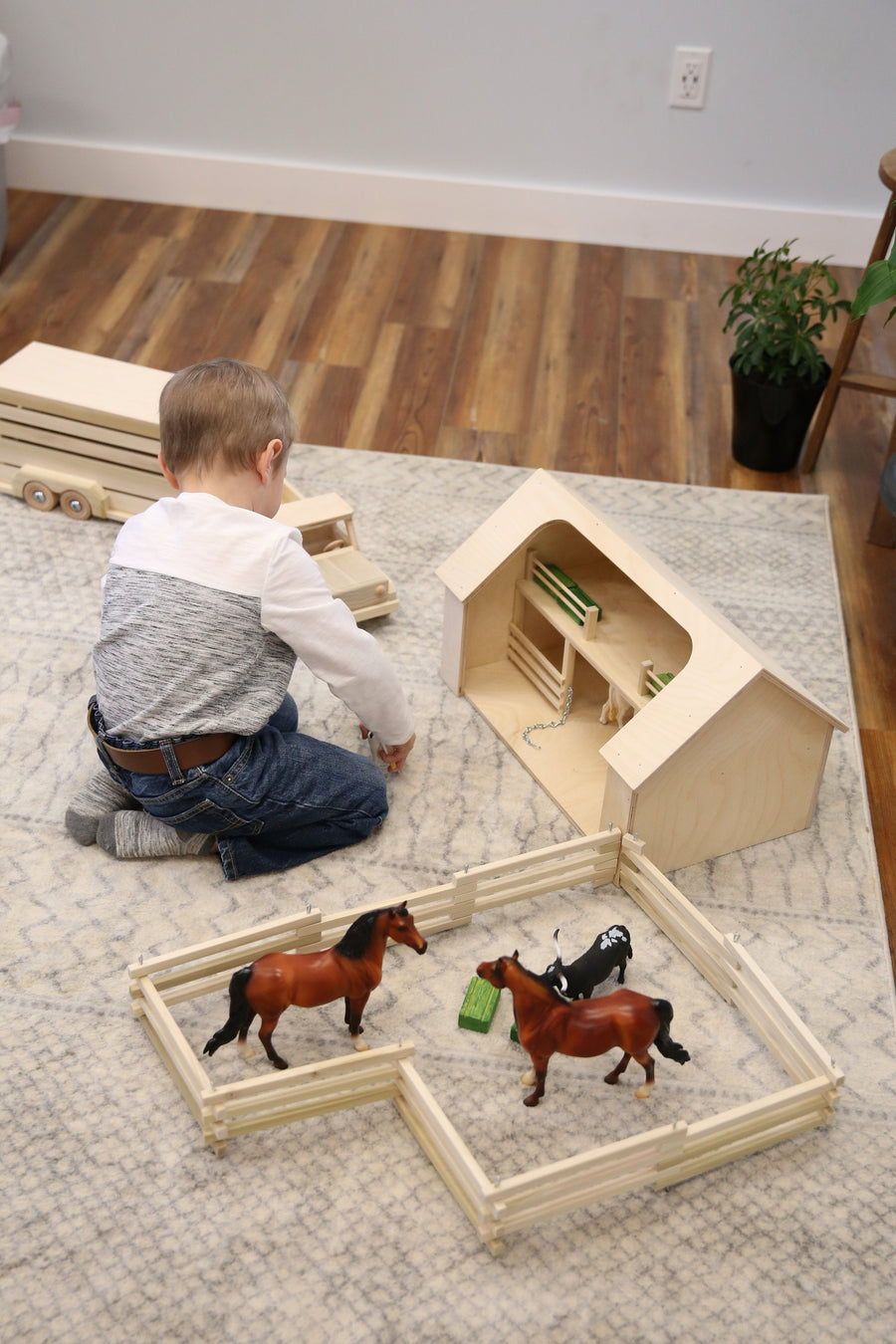 Child arranging toy animals inside a folding wooden fence