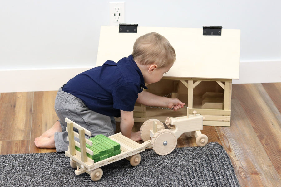 Child playing with a wooden tractor, hay wagon and hay bales