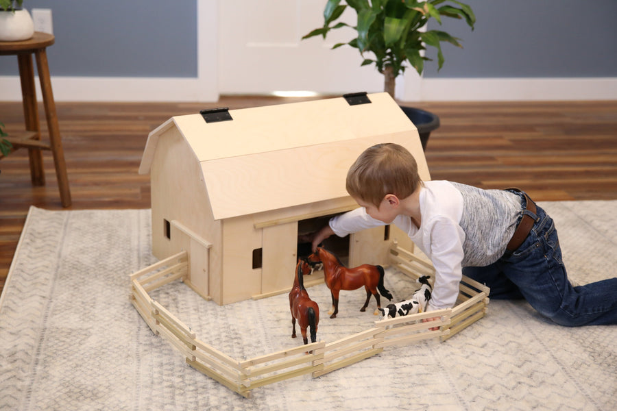 Child arranging toy animals inside a folding wooden fence