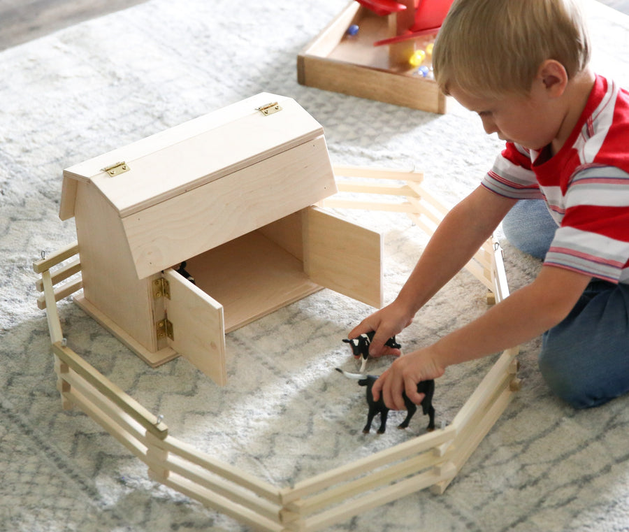 Child playing with a miniature wooden hip-roof barn