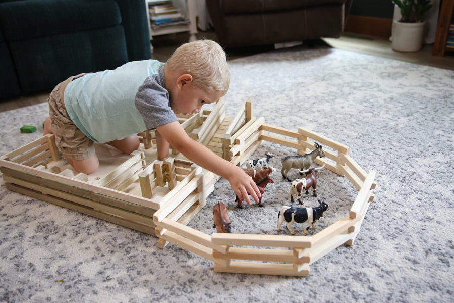 Child arranging a farm scene with a folding wooden corral fence