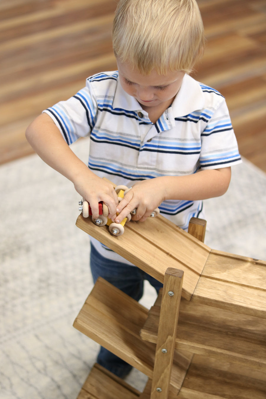 Child setting cars on a wooden roller racetrack