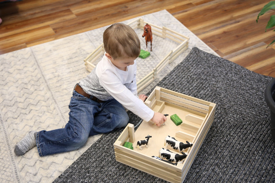 Child arranging toy animals inside a wooden miniature stockyard