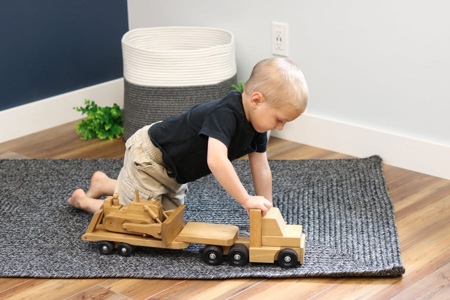 Child playing with a wooden truck and construction-vehicle trailer