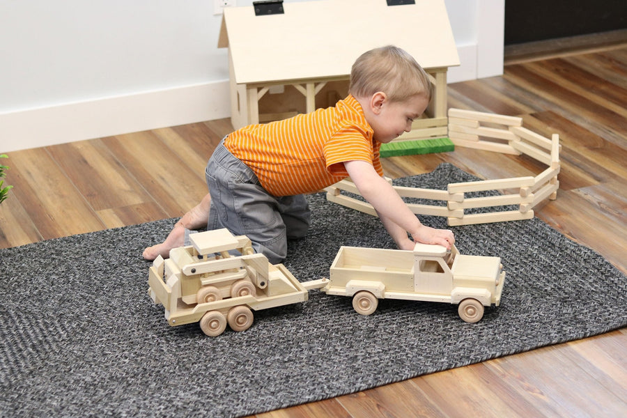 Child playing with a wooden pickup, equipment trailer and skid loader