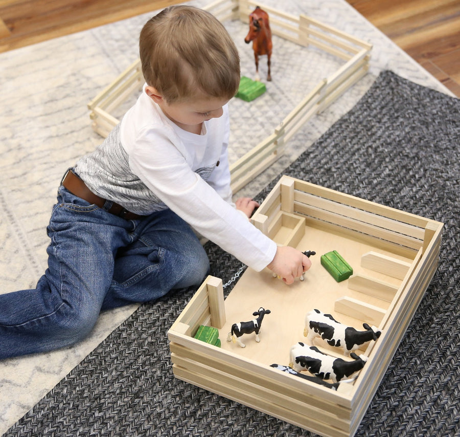 Child arranging toy animals inside a wooden miniature stockyard