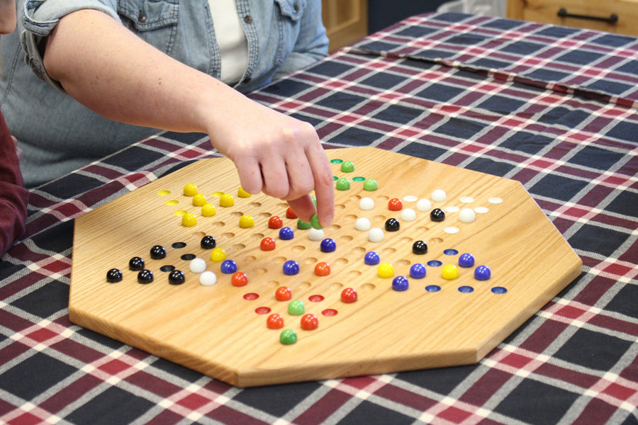 Players moving marbles on an oak Chinese Checkers board