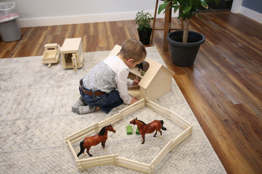 Child playing with a wooden ranch shed and farm animals
