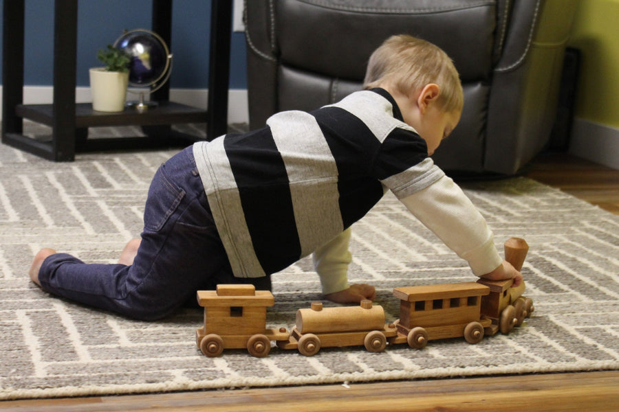 Child playing with a linked wooden toy train on a rug