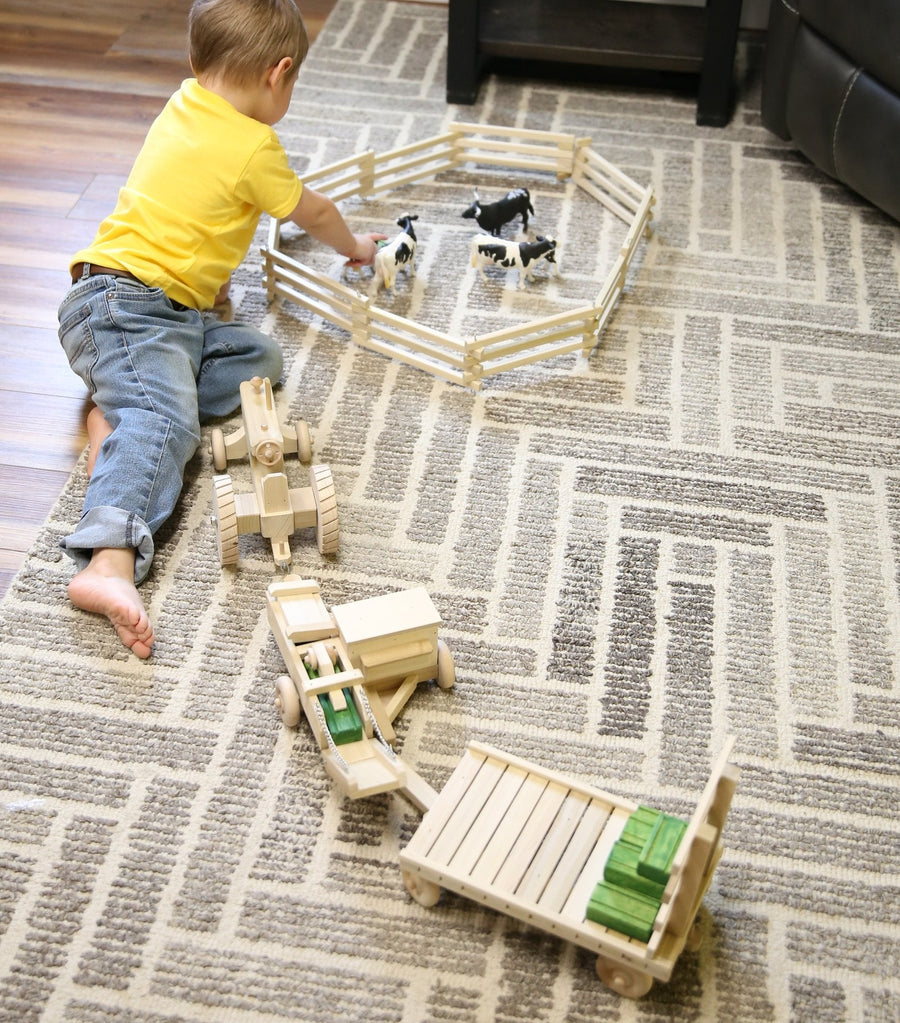 Child playing with a wooden tractor, baler and hay wagon