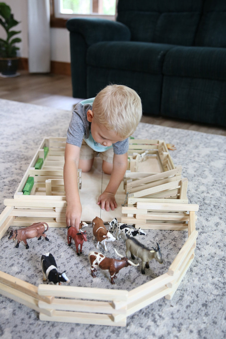 Child arranging a farm scene with a folding wooden corral fence
