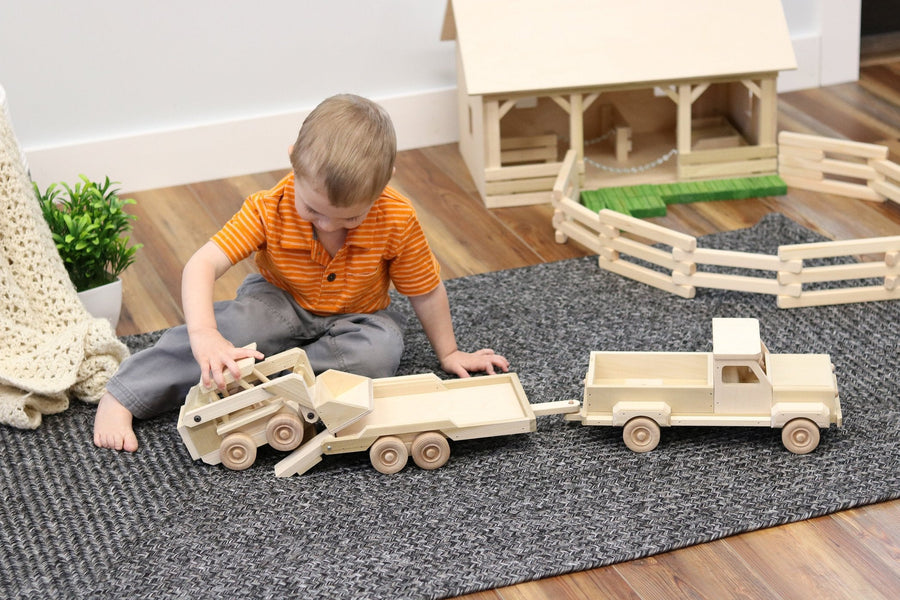 Child playing with a wooden pickup, equipment trailer and skid loader