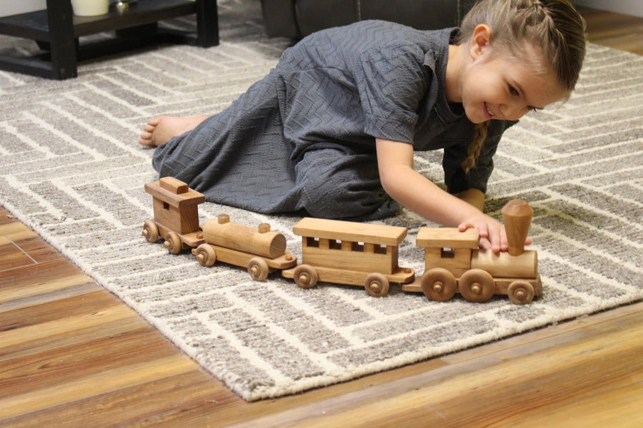 Child playing with a linked wooden toy train on a rug