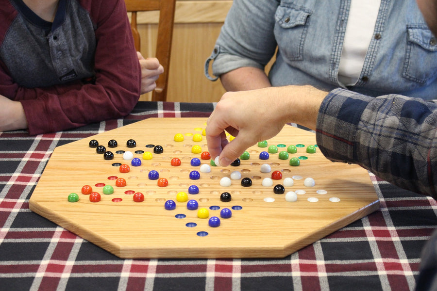 Players moving marbles on an oak Chinese Checkers board