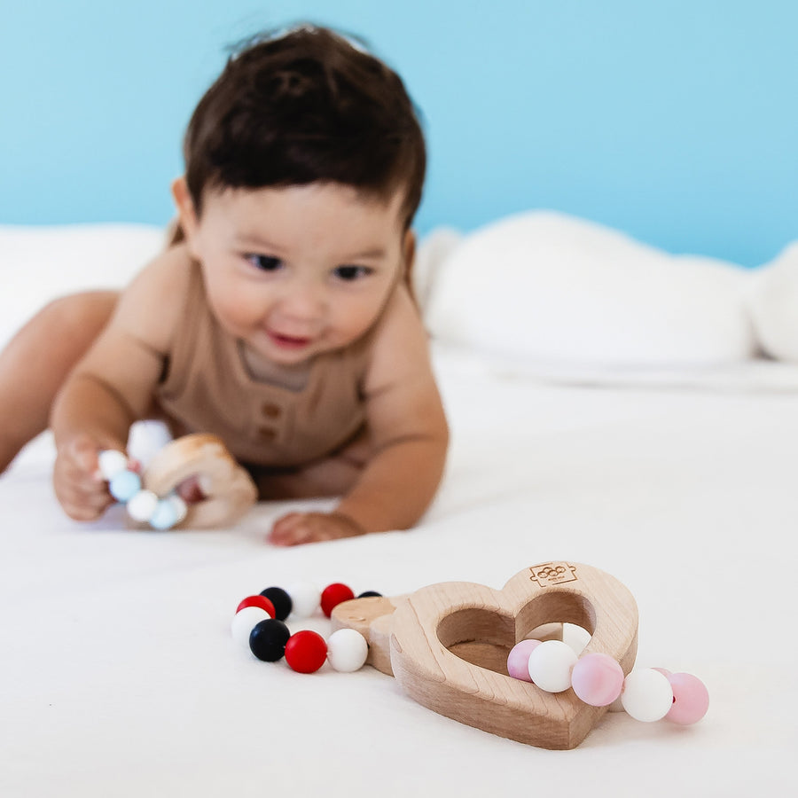 Baby holding a wooden teether with silicone beads during supervised play