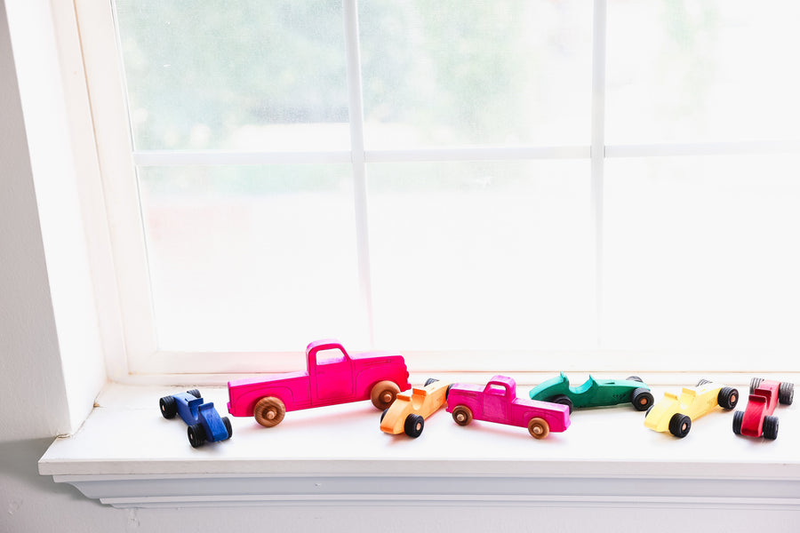 Colorful wooden toy pickup trucks lined up on a windowsill