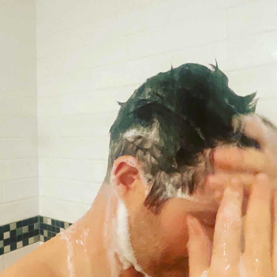 Person rinsing shampoo from hair in a shower