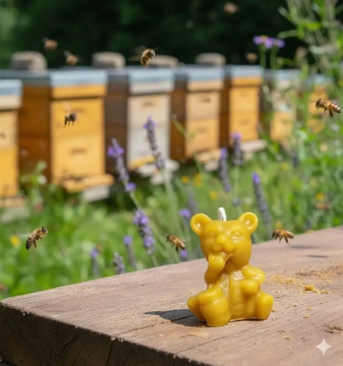 Small golden bear-shaped beeswax candle with a wick on a wooden surface in front of beehives
