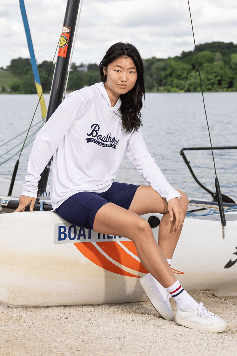 Boathouse Logo UPF 50+ Sun Hoodie: model wearing white sun hoodie beside a car.